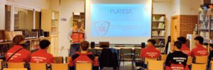TES en chaleco naranja impartiendo charla PLATESA a jóvenes de Urgencias y Protección Civil en biblioteca